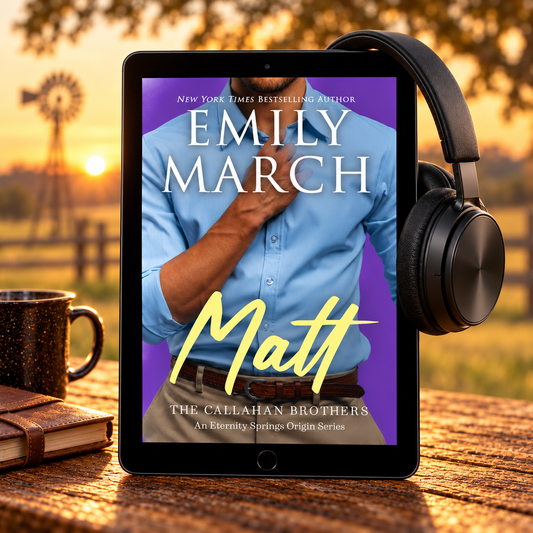 A tablet on a wooden table displaying a romance novel cover for 'Matt' by Emily March, with black over-ear headphones resting on the right side and a mug and notebook on the left, set against a warm outdoor sunset background.